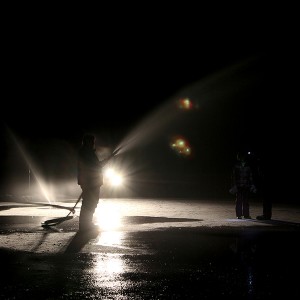 Light from the quad illuminates Rick O'Neill as he floods the rink with a fire hose.
